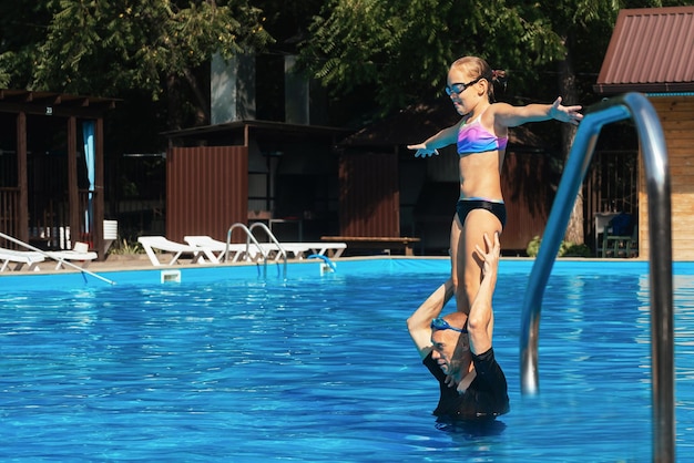De coach leert het meisje om haar evenwicht te bewaren en vanaf haar schouders in het water van het zwembad te duiken