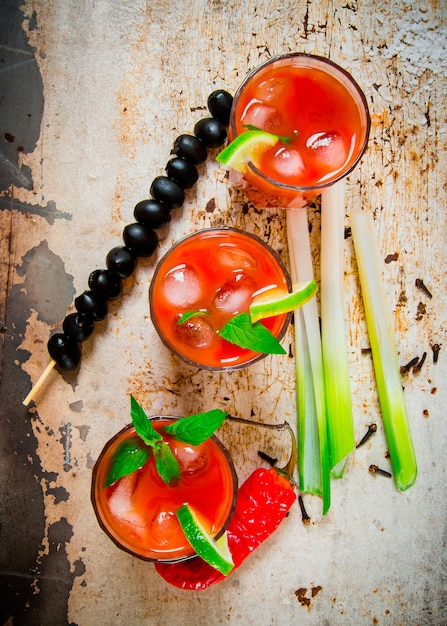 De cocktail bloody mary. cocktails gemaakt van tomaten, alcohol, ijs, limoen, peper, zout en snack met selderij en zwarte olijven op rustieke tafel. bovenaanzicht