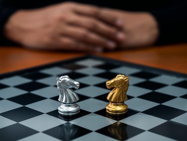 Foto de confrontatie tussen gouden en zilveren paarden ridder schaakstuk staan samen op het schaakbord met speler achter leiding partnerschap concurrent concurrentie en bedrijfsstrategie concept