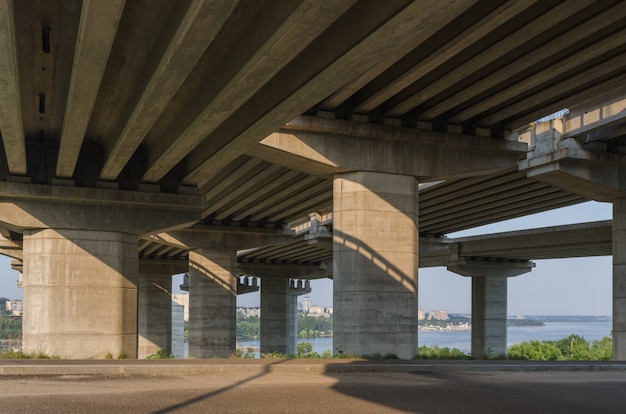 De constructie van een brug over de rivier met de steunen, structurele elementen, kranen