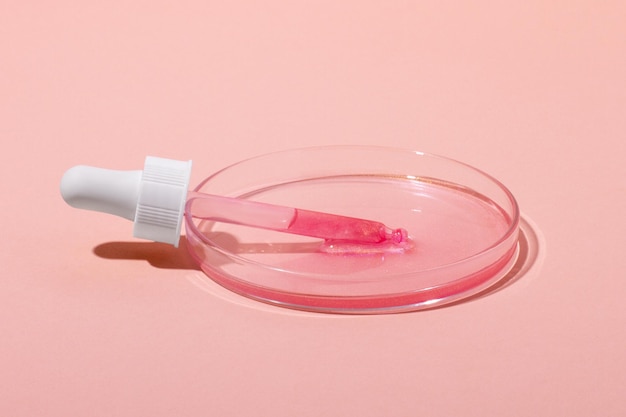 De cosmetische pipet ligt in een petrischaaltje met roségoud Of een roze vloeistof met glitters Laboratoriumonderzoek naar cosmetica gelgeneeskunde Chemie