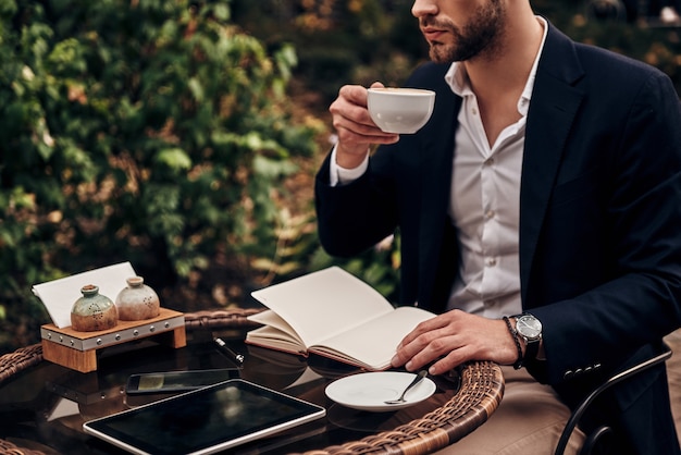 De dag plannen. Close up van een jonge man in slimme vrijetijdskleding die koffie drinkt terwijl hij buiten in het restaurant zit