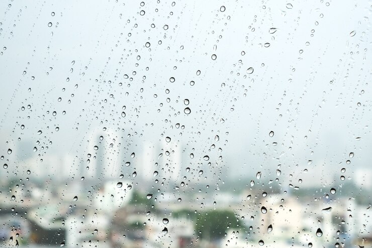 De dalingen van de waterregen op vensterglas met witte grijze bewolkte stadsachtergrond.