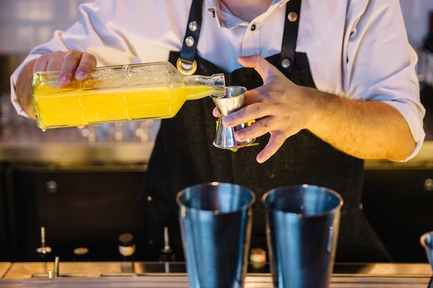 De deskundige barman maakt cocktail met geel sap bij nachtclub