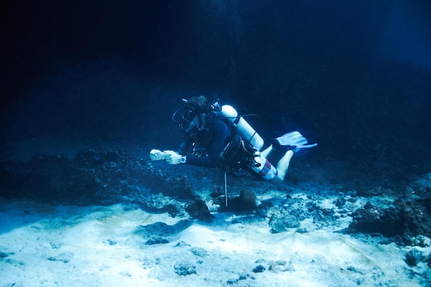 De diepten van de donkere oceaan trotseren Mannelijke duiker die net boven de oceaanbodem drijft Diepzeeduiken
