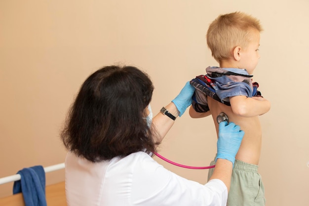 De dokter gebruikt een stethoscoop op de rug van de jongen om zijn gezondheid te controleren