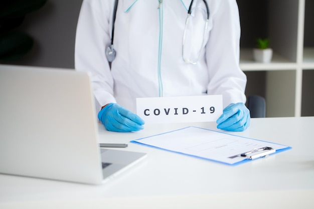 De dokter houdt een kaart met het Covid-symbool in het kantoor van de kliniek