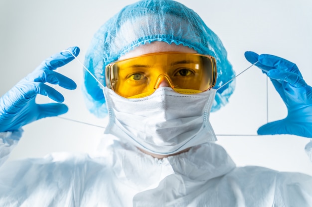 De dokter in een beschermend pak zet een masker op. Coronavirus-epidemie in 2020