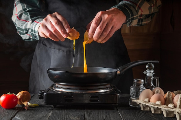 De dooier valt in een koekenpan van een gebarsten rauw ei, gespleten door de handen van de kok. werkomgeving in de restaurantkeuken