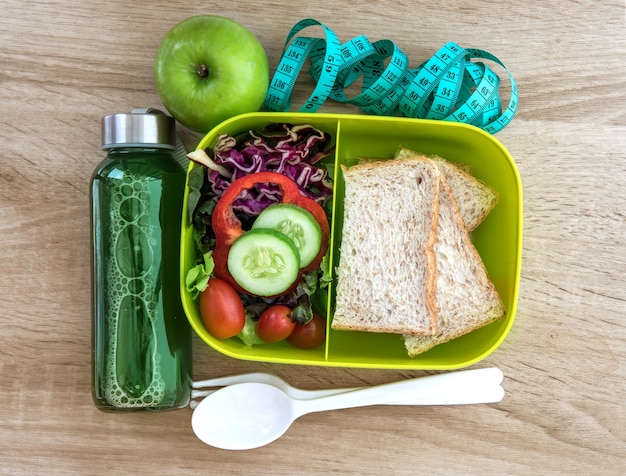 De doos van de gezonde lunch met graan brood en groene groente