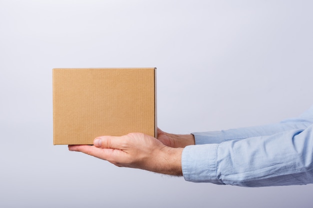 Foto de doos van de mensenholding at arm's length op witte muur. vierkante kartonnen doos. levering van pakketten. zijaanzicht.