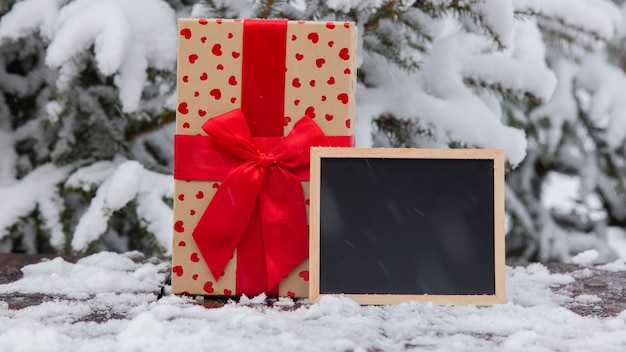 De doos van de vakantiegift met hartvormen en bord op houten lijst in sneeuw