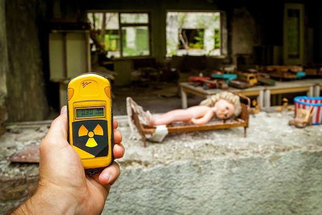 De dosismeter in de handen met het niveau van radioactiviteit in het verlaten gebouw van de kleuterschool na de explosie van de Pripyat-reactor, Tsjernobyl.