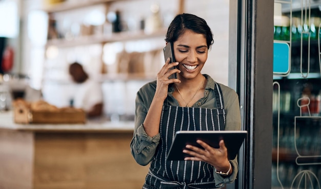 De draadloze barista-opname van een jonge vrouw die een digitale tablet en smartphone gebruikt terwijl ze in een café werkt