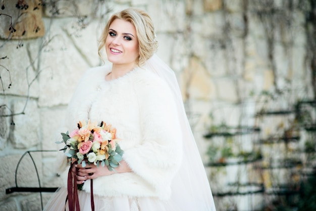 Foto de dromerige blondebruid in witte laag houdt huwelijksboeket in haar wapens