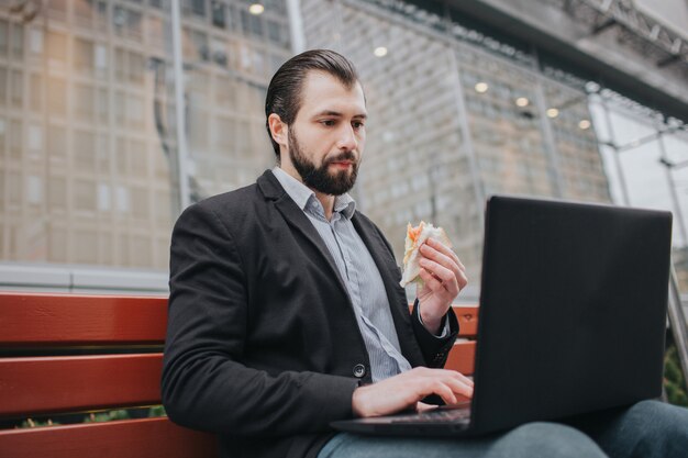 De drukke man heeft haast, hij heeft geen tijd, hij gaat onderweg snacks eten. Werknemer eten, koffie drinken, praten aan de telefoon, tegelijkertijd. Zakenman doet meerdere taken.