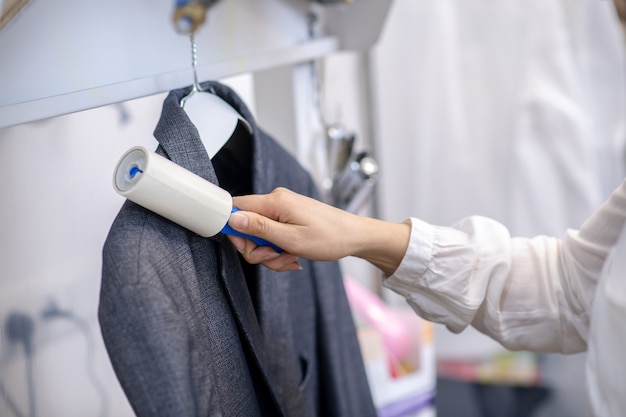 De dunne hand van de vrouw met een pluizenroller die donkergrijs hangend jasje aanraakt