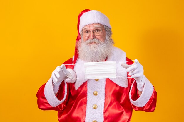 De echte kerstman met een gele achtergrond, met een beschermend masker, bril en hoed. Kerst met sociale afstand. Covid-19