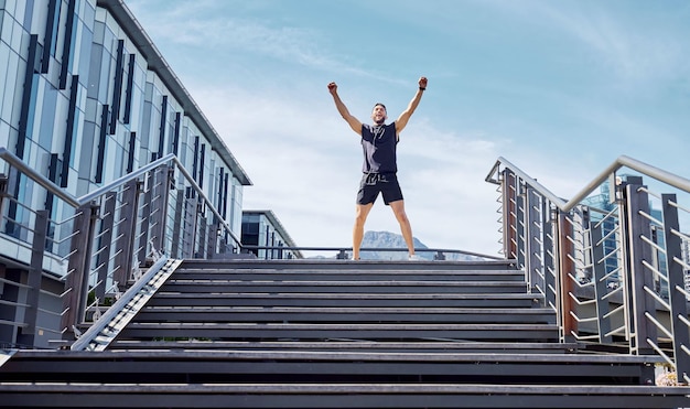 De eerste plaats is voor mij. Lage hoekopname van een sportieve jongeman die juicht op de top van een trap terwijl hij buiten aan het sporten is.