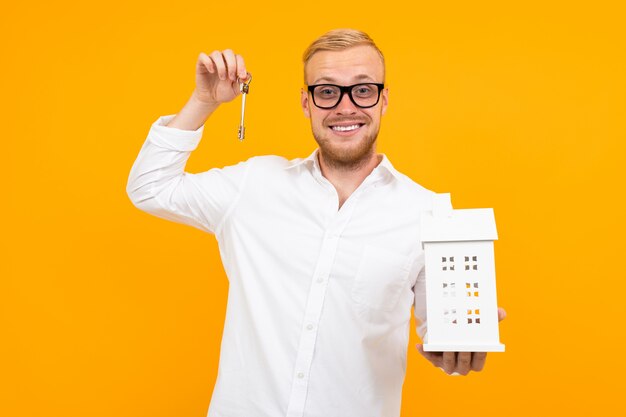 De eigenaar van het pand houdt een huismodel en sleutels in zijn hand op een geel met kopie ruimte