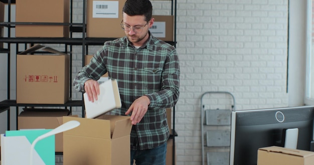 De eigenaar verpakt boeken die online aan een klant zijn verkocht Voorbereiding van een kleine kartonnen doos voor verzending Een jonge manager werkt in een magazijn