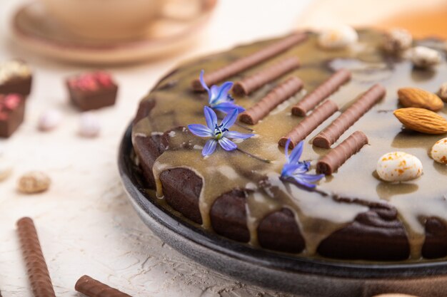 De eigengemaakte cake van de chocoladebrownie met karamelroom en amandelen met kop van koffie op een witte concrete achtergrond.