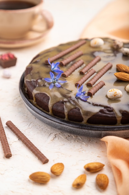 De eigengemaakte cake van de chocoladebrownie met karamelroom en amandelen met kop van koffie op een witte concrete achtergrond.