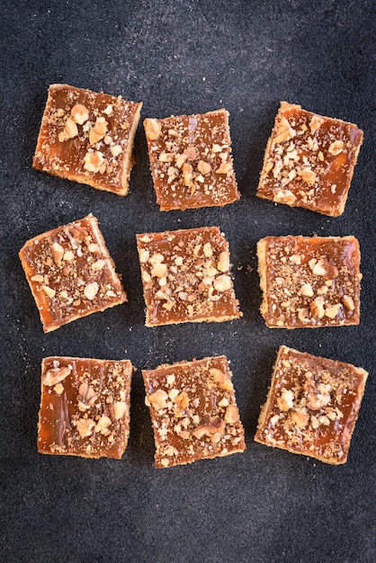 De eigengemaakte karamelzandkoek regelt koekjes met noten die in de vorm van een vierkant op zwarte achtergrond met kruimels worden gelegd.