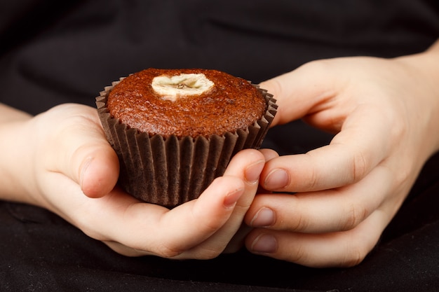 De eigengemaakte muffin van de chocoladebanaan in de handen van kinderen