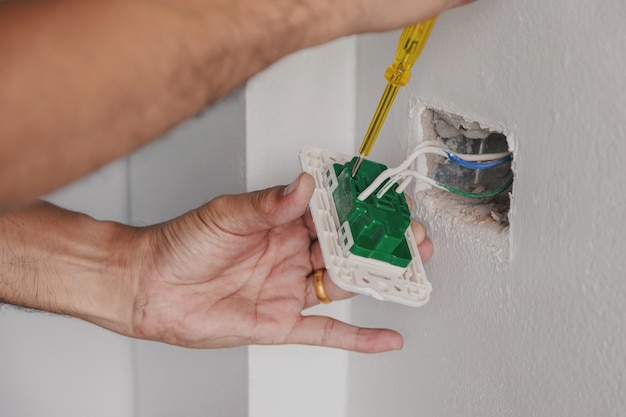 De elektricien gebruikt een schroevendraaier om de stekker op de muur te controleren.