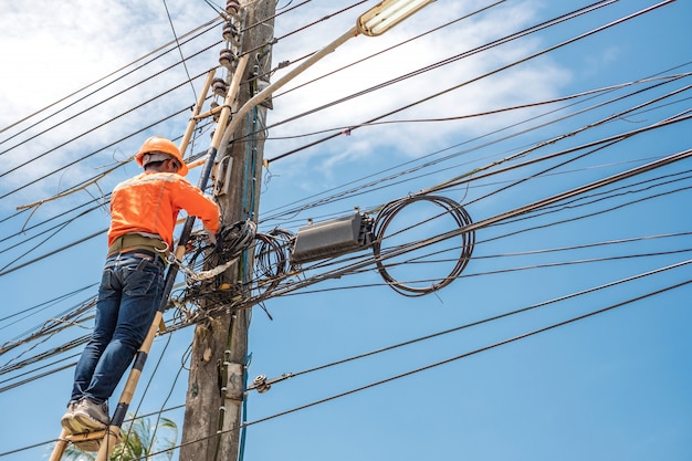 De elektrische lijnwachterarbeider beklimt een bamboeladder om draad te herstellen