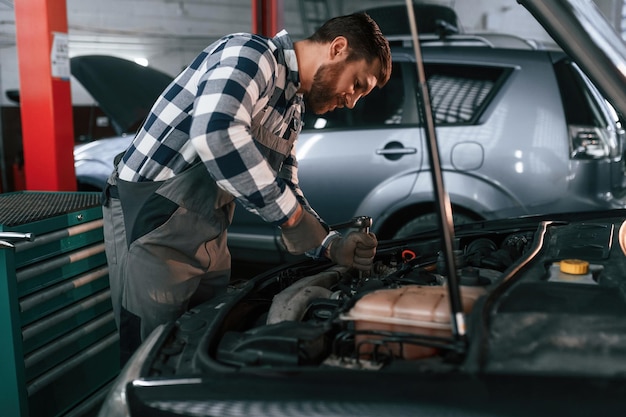 De elektronica van de auto onder de motorkap repareren Man in uniform werkt in de autosalon