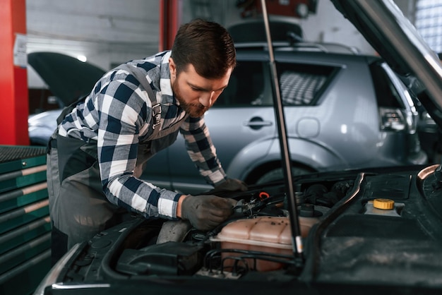 De elektronica van de auto onder de motorkap repareren Man in uniform werkt in de autosalon