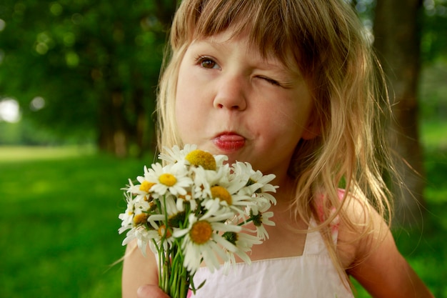 De emoties van het kind die tong tonen gelukkig meisjeskind met een boeket van bloemen in het natuurpark