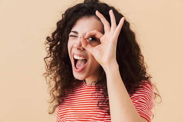 Foto de emotionele jonge krullende vrouw maakt oke gebaar.