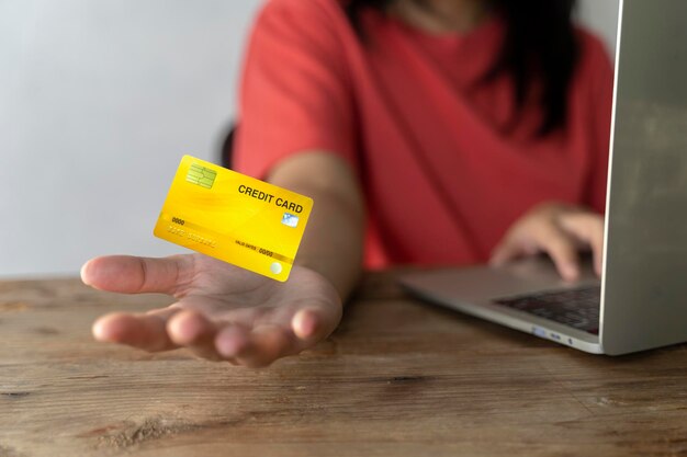 De ene hand houdt een creditcard vast en de andere hand voert de bestelling in op een computerlaptop met een winkelwagentje als achtergrond