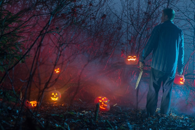 De enge mens in nachtbos snijdt Halloween-pompoenen