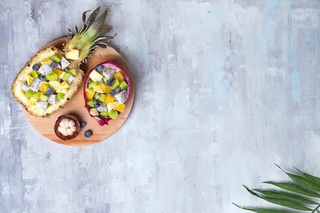 De exotische fruitsalade diende in de helft van een draakfruit en een ananas op ronde houten plaat op steenachtergrond, exemplaarruimte. Bovenaanzicht