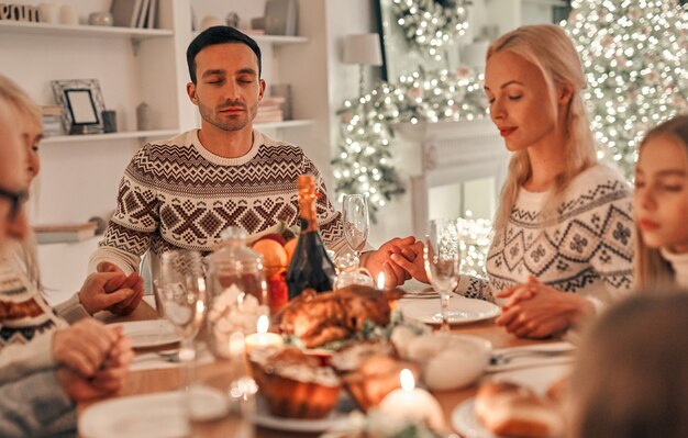 De familie aan het bidden aan de kersttafel