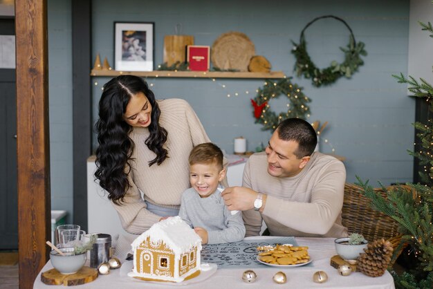 De familie bakt een peperkoekhuis voor kerstmis met snoep dat de vader glazuur doet