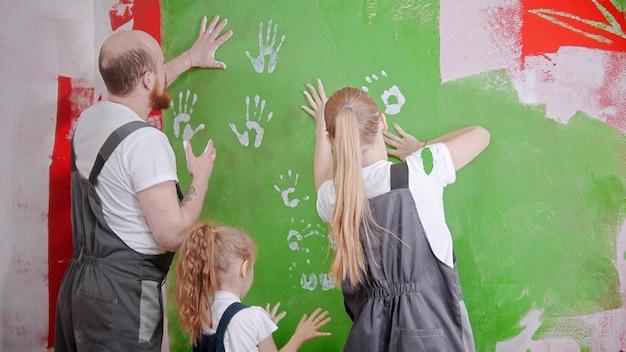 De familie in overall met rollers schildert een witte muur met groene verf