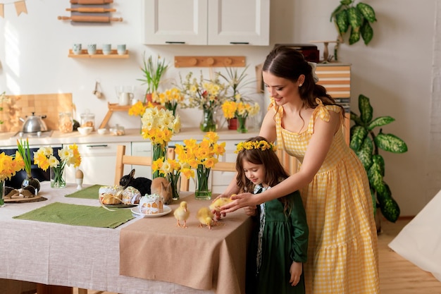 De familie viert Pasen, mooi meisje en haar jonge moeder thuis in de keuken bij de feesttafel met paascakes en eendjes