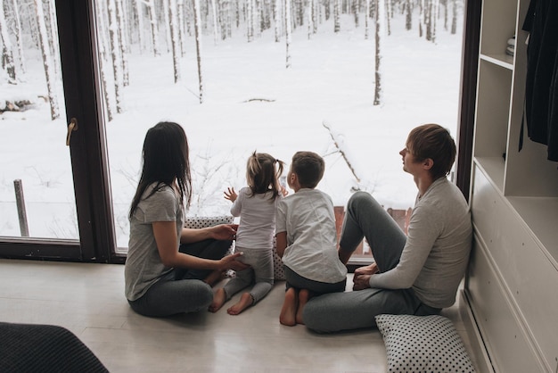 De familie zit bij het raam en kijkt naar het winterbos. Goede nieuwjaarsgeest. Ochtend in pyjama.