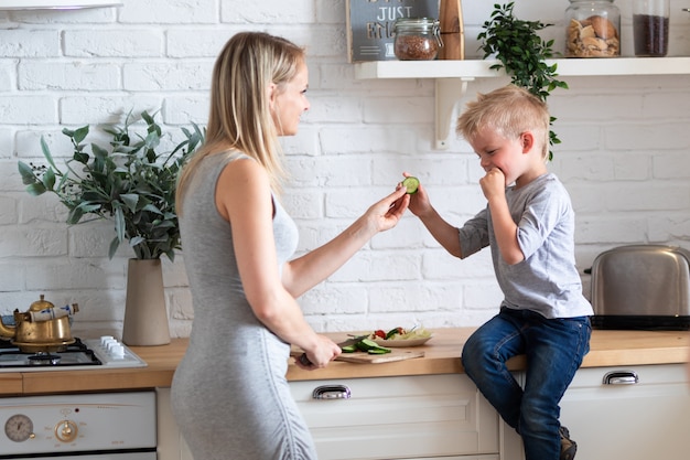 De familiemoeder en zoon die van de blonde gezond voedsel in keuken thuis eten, groene salade op platen