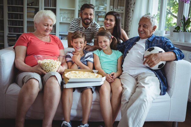 De familiezitting van meerdere generaties met popcorn en pizza terwijl het bekijken van voetbalwedstrijd