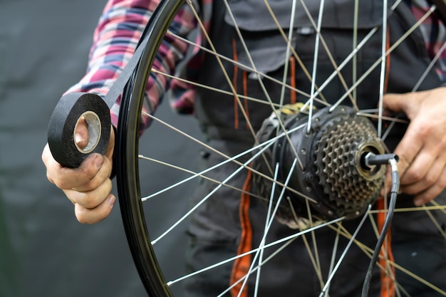 De fietsenmaker houdt het achterwiel van de elektrische fiets en het velglint in zijn hand Bescherming van de fietscamera tegen lekke banden, snijwonden en wrijving Professionele fietsreparatie