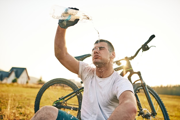 De fietser zit in een weiland terwijl hij uitrust van een inspannende rit over bergwegen. De fietser wordt gekoeld door water. Selectieve focus. Hoogwaardige foto