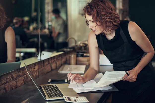 De financiële kant van de zaak lijkt in orde. Shot van een aantrekkelijke jonge kapper die staat en haar laptop gebruikt terwijl ze haar financiën in haar salon berekent