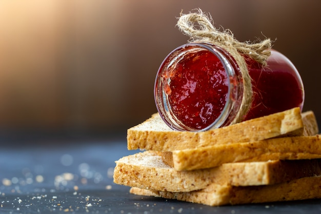 De fles van de aardbeijam en het gehele tarwebrood worden gestapeld op een zwarte achtergrond