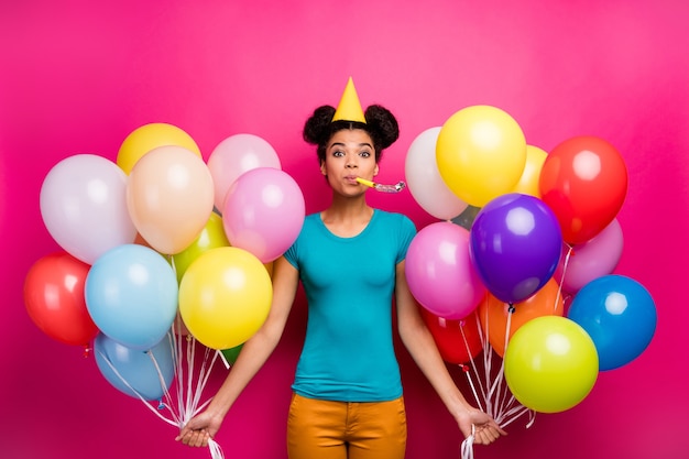 De foto van vrij grappige dame houdt vele kleurrijke luchtballons blaast noisemaker